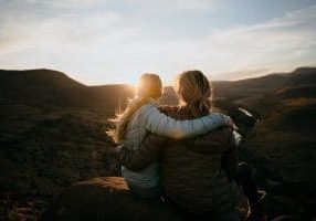 Caucasian Mother and Daughter bonding and hugging while enjoying the beautiful view after a mountain hike during sunset.